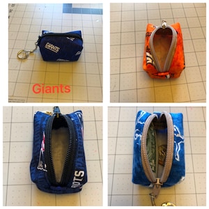 May include: Four zippered pouches featuring different team logos. The pouches are made of fabric and have a zipper closure. The logos are for the New York Giants, the New York Jets, and the New England Patriots. All pouches are open, revealing the soft fabric lining inside.