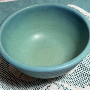 May include: A small, round ceramic bowl with a matte finish in a vibrant turquoise blue color. The interior of the bowl features a subtle gradient, transitioning from a deeper blue at the rim to a lighter, pale green hue at the base.