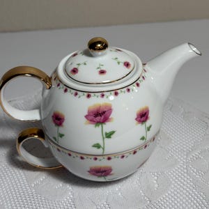 Peut inclure: Un service à thé en porcelaine blanche composé d'une théière empilée sur une tasse. L'ensemble est orné de fleurs de coquelicot roses et jaunes, de tiges vertes et de petites bordures florales roses. Le couvercle et les anses ont des dorures.