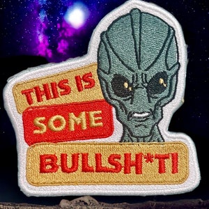 May include: A white, gold, and red embroidered patch with a gray alien face and the text "This is some BULLSH*T!"