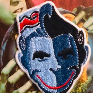 May include: A blue and black embroidered patch of a face with a red smile. The face is split in half, with one side blue and the other black.