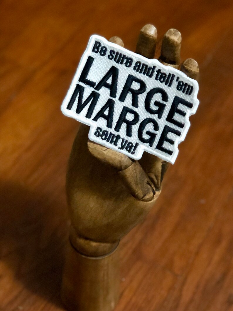 K&ouml;nnte beinhalten: Ein rechteckiger gestickter Aufn&auml;her mit wei&szlig;em Hintergrund und schwarzem gesticktem Rand. Der Aufn&auml;her zeigt den schwarzen gestickten Text "Be sure and tell 'em LARGE MARGE sent ya!" in einer fetten, serifenlosen Schriftart auf der Oberfl&auml;che.