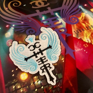 May include: A white and blue embroidered patch with a cross and wings. The patch has the words "Living Proof" and "Tour 200" on it.