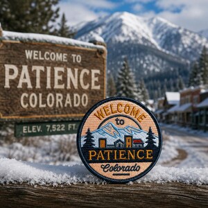 May include: A circular embroidered patch featuring a mountain landscape, pine trees, and buildings with the text Welcome to PATIENCE Colorado. The patch has a tan background, dark blue border, and colorful thread details depicting a snowy town scene.
