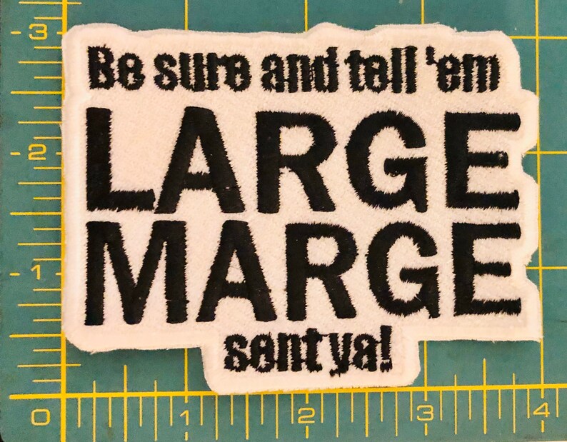 K&ouml;nnte beinhalten: Ein rechteckiger, wei&szlig;er, bestickter Aufn&auml;her mit schwarzem Text, der "Be sure and tell 'em LARGE MARGE sent ya!" lautet. Der Aufn&auml;her liegt auf einer gr&uuml;nen Schneidematte mit gelbem Raster und ist etwa 9 cm breit.