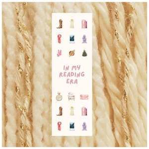 May include: A white bookmark featuring watercolour illustrations of a cowboy boot, dress, books, scarf, mountain scene, planet, Christmas tree, pocket watch, chair, and a jewelry box. The text "IN MY READING ERA" is in pink.