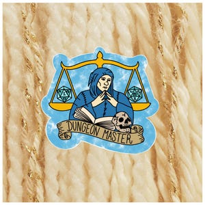 May include: A blue sticker featuring a robed figure with hands clasped, a skull, and dice. The figure is positioned under a golden scale, with the words "DUNGEON MASTER" on a banner below.