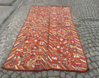 May include: A large, rectangular rug with a colorful geometric pattern. The rug is made of wool and has a fringe border. The colors in the rug are red, orange, yellow, blue, and green.