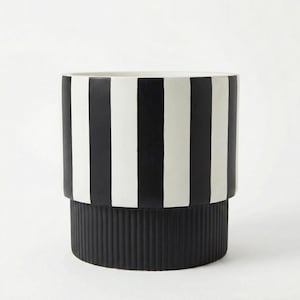 May include: A cylindrical black and white striped planter. The upper portion features vertical black stripes against a white background. The base is solid black with a ribbed texture. A modern decorative item.