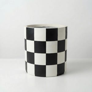 May include: A cylindrical planter with a black and white checkerboard pattern. The planter has a wide, rounded rim and a smooth, matte finish. The black squares alternate with white squares, creating a bold, graphic design. The planter is suitable for indoor or outdoor use.
