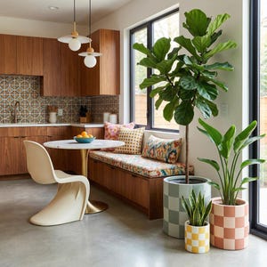 May include: A modern kitchen with wooden cabinets, a round marble table, and a unique cream-colored chair. A built-in bench with patterned cushions sits by a window, and several potted plants in checkered pots add a touch of greenery.