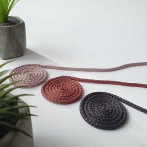 May include: Three coiled rope trivets in pink, red, and grey. The trivets are made of braided rope and are perfect for protecting surfaces from heat.