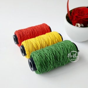May include: Three spools of colorful string, red, yellow, and green, are arranged in a row. The spools are made of a natural material and have a simple design.