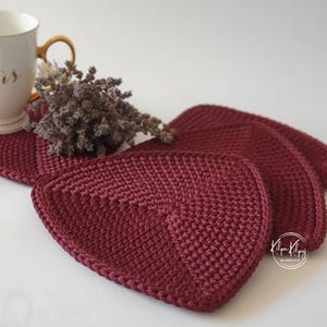 May include: Set of four maroon crocheted coasters. The coasters are shaped like rounded squares with a textured surface.