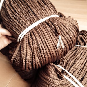 May include: Two spools of brown cord wrapped with white tape. The cord is tightly wound and has a rough texture.