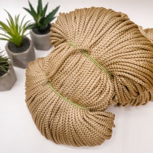 May include: A large spool of thick, brown cotton rope. The rope is tightly wound and has a green band around it.