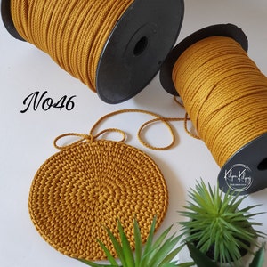 May include: Two spools of mustard yellow cotton rope, one with a black label and the text "N046", and a crocheted coaster made from the same rope.