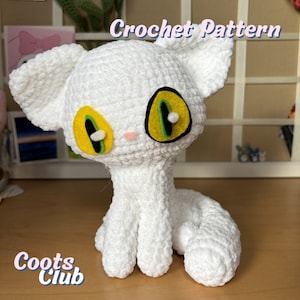 Può includere: Un amigurumi di gatto bianco all'uncinetto con occhi verdi e gialli. Il gatto è seduto su una superficie di legno. Il testo "Crochet Pattern" è nell'angolo in alto a destra dell'immagine. Il testo "Coots Club" è nell'angolo in basso a sinistra dell'immagine.
