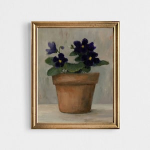 May include: A painting of a potted violet plant with purple flowers and yellow centres. The plant is in a terracotta pot and is sitting on a light grey surface. The painting is framed in a gold frame.
