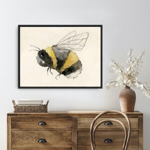 May include: Watercolor painting of a bumblebee with black and yellow stripes and translucent wings on a cream background.