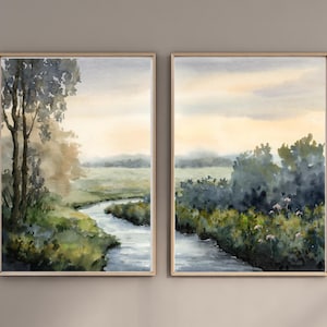 May include: Two framed watercolor landscape paintings. Each features a river winding through a green and yellow field, with trees and bushes along the banks. The sky is a soft yellow and gray.