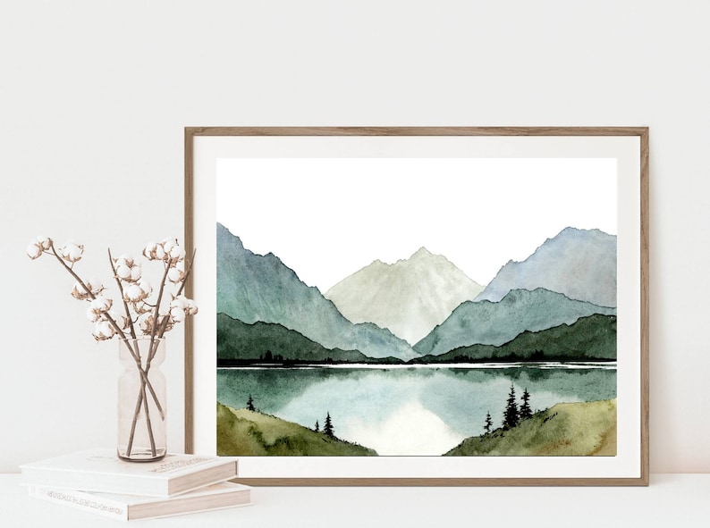 May include: Watercolor painting of a mountain range with a lake in the foreground. The mountains are painted in shades of green and blue, and the lake is a light blue. The painting is framed in a wooden frame.