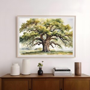 May include: Watercolor painting of a large oak tree with sprawling branches and lush green foliage. The artwork is framed in a light wood frame and hangs above a wooden cabinet. Decorative vases and books are on the cabinet.