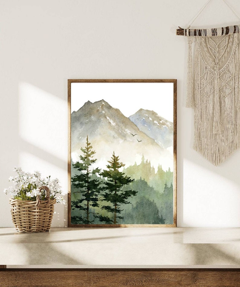 May include: A watercolor painting of a mountain range with a forest in the foreground. The mountains are painted in shades of gray and blue, while the forest is painted in shades of green. The painting is framed in a brown frame.