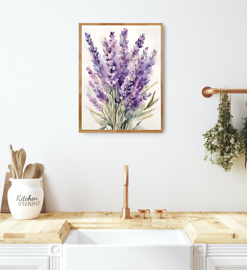 May include: A framed watercolour painting of lavender flowers. The artwork, in shades of purple and green, has a soft, artistic style. The painting is displayed on a white wall, suggesting a home decor theme. The frame is made of wood.