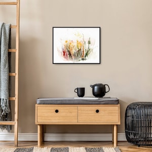 K&ouml;nnte beinhalten: Ein gerahmtes Aquarellbild eines Feldes mit Wildblumen in Gelb-, Orange-, Rot- und Gr&uuml;nt&ouml;nen. Das Bild h&auml;ngt an einer hellbeigen Wand &uuml;ber einer Kommode aus Holz mit zwei Schubladen.