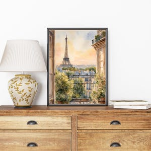 K&ouml;nnte beinhalten: Ein Aquarellbild eines Pariser Balkons mit Blick auf den Eiffelturm in der Ferne. Das Bild ist in einem schwarzen Rahmen gerahmt und h&auml;ngt an einer Wand.