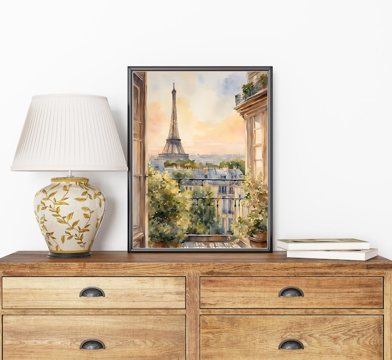 K&ouml;nnte beinhalten: Ein Aquarellbild eines Pariser Balkons mit Blick auf den Eiffelturm in der Ferne. Das Bild ist in einem schwarzen Rahmen gerahmt und h&auml;ngt an einer Wand.