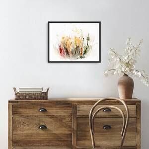 K&ouml;nnte beinhalten: Ein gerahmtes Aquarellbild eines Feldes mit Wildblumen in Gelb-, Orange-, Rot- und Gr&uuml;nt&ouml;nen. Das Bild hat einen wei&szlig;en Hintergrund und ist in Schwarz gerahmt.