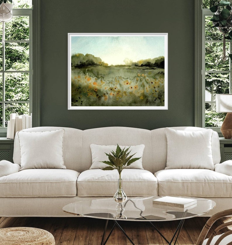 May include: A watercolor painting of a field of wildflowers with a green background and a blue sky. The painting is framed in a white frame and is hanging on a green wall.