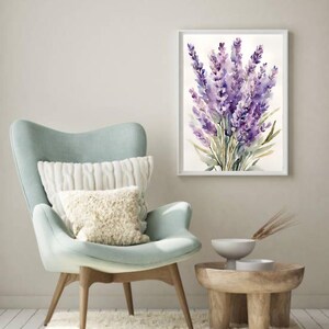 May include: A framed watercolour painting of lavender flowers. The artwork hangs above a light blue armchair with white cushions. A small wooden side table with a white bowl and decorative items is placed nearby.