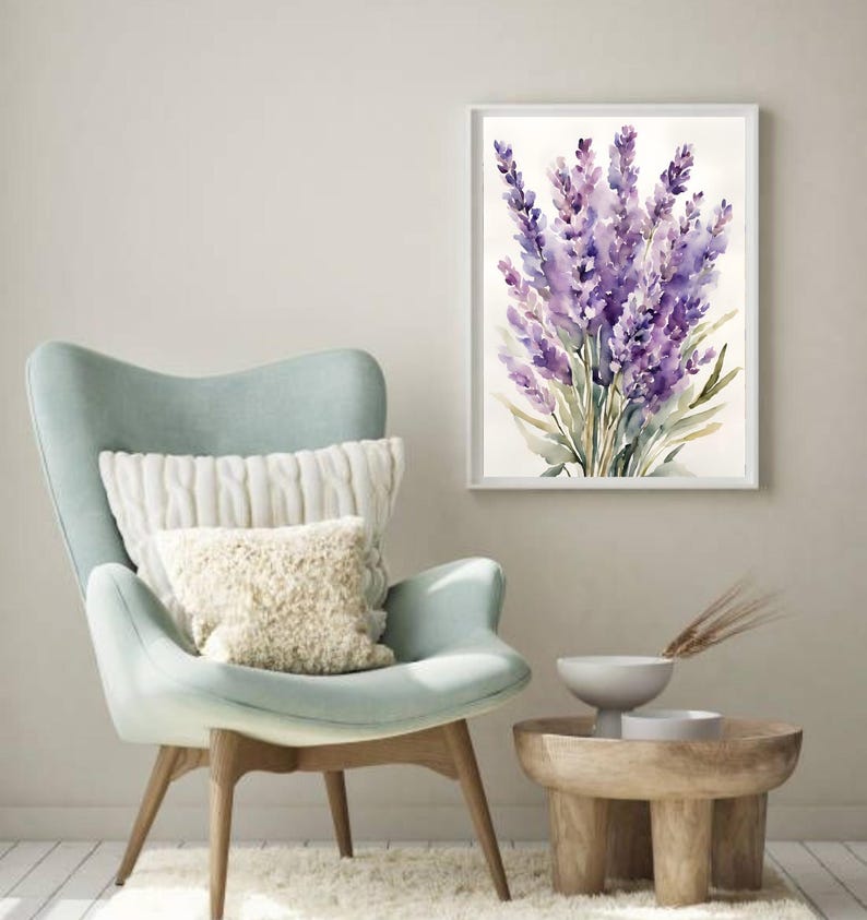 May include: A framed watercolour painting of lavender flowers. The artwork hangs above a light blue armchair with white cushions. A small wooden side table with a white bowl and decorative items is placed nearby.