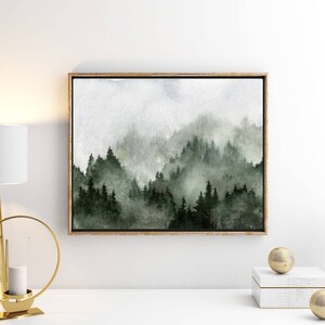 May include: A watercolour painting of a misty forest scene with green trees and a light grey sky. The painting is framed in a light wood frame.