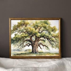 May include: Watercolor painting of a large oak tree with a wide canopy of green and yellow leaves. The tree's trunk and branches are brown. The artwork is framed in a gold-colored frame, set against a neutral background.