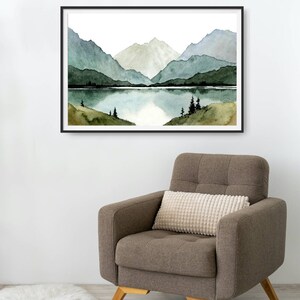 May include: A framed watercolor painting of a mountain lake scene. The painting features a lake surrounded by mountains with a reflection of the mountains in the water. The mountains are painted in shades of green and blue.