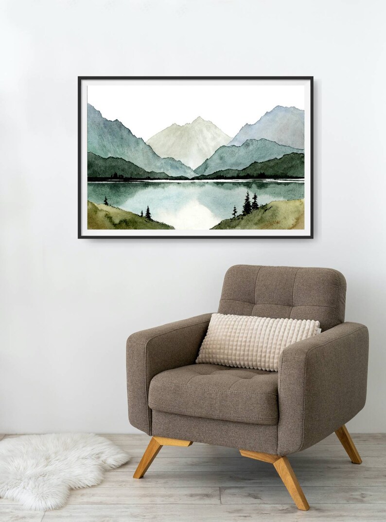 May include: A framed watercolor painting of a mountain lake scene. The painting features a lake surrounded by mountains with a reflection of the mountains in the water. The mountains are painted in shades of green and blue.