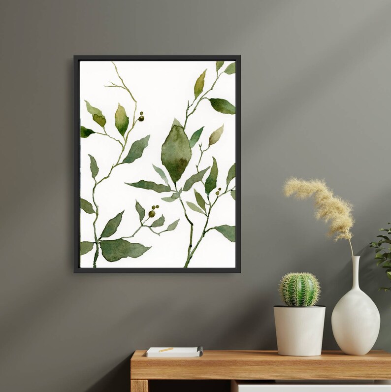 Puede incluir: Una pintura de acuarela enmarcada de hojas y ramas verdes sobre un fondo blanco. La pintura est&aacute; en un marco negro y est&aacute; colgada en una pared gris.