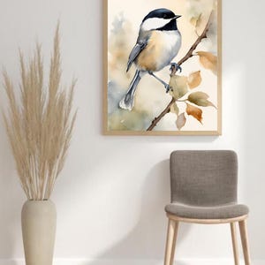 May include: A watercolor painting of a black-capped chickadee perched on a branch with brown leaves. The bird is facing the right side of the image and has a light brown body with a black cap and bib. The background is a soft watercolor wash of light brown and blue.