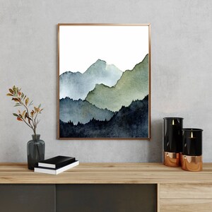 Pu&ograve; includere: Un dipinto ad acquerello incorniciato di una catena montuosa in tonalit&agrave; di blu, verde e nero. Le montagne sono rappresentate in modo stilizzato e astratto, con bordi morbidi e linee fluide. Il dipinto &egrave; su uno sfondo bianco.