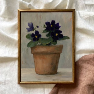 May include: A painting of a potted violet plant with purple flowers in a terracotta pot. The plant is sitting on a white surface with a light gray background.