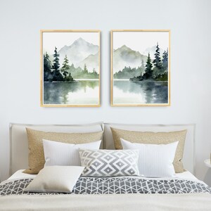 May include: Two framed watercolor paintings of a misty mountain lake scene with green trees and a reflection of the mountains in the water.