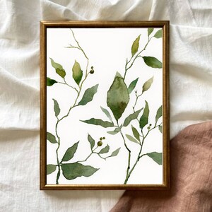 Puede incluir: Una pintura de acuarela enmarcada de hojas verdes y ramas sobre un fondo blanco. Las hojas est&aacute;n pintadas en un estilo suelto y abstracto, y las ramas son delgadas y delicadas.