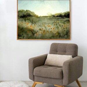 May include: A framed watercolor painting of a field with green trees and yellow flowers in the foreground. The sky is a light blue with a hint of orange in the distance.