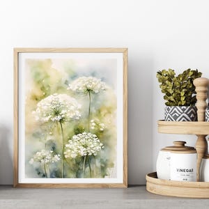 May include: A watercolour painting of white Queen Anne's Lace flowers against a green and yellow background. The painting is framed in a light wood frame.