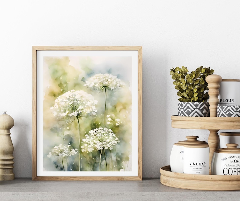 May include: A watercolour painting of white Queen Anne's Lace flowers against a green and yellow background. The painting is framed in a light wood frame.