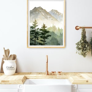 May include: A watercolor painting of a mountain landscape with two pine trees in the foreground. The mountains are a muted green and gray, and the sky is a light blue. The painting is framed in a light wood frame.